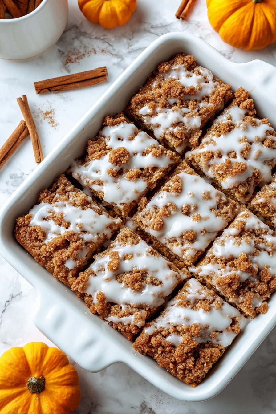 A close-up view of a white baking dish filled with a brown crumbly baked dessert that has been lightly drizzled with white glaze on top. The dessert is already sliced into squares, showing a rough, crunchy texture. The brown crumb topping is uneven and chunky, with the white glaze spread thinly and randomly over the surface. Around the dish, there are cinnamon sticks and small orange pumpkins on a white marbled surface. Photo taken with an iphone --ar 2:3 --v 7 - Pumpkin Coffee Cake with Cinnamon Streusel and Vanilla Drizzle, pumpkin coffee cake, fall coffee cake recipes, pumpkin spice cake, cinnamon streusel dessert