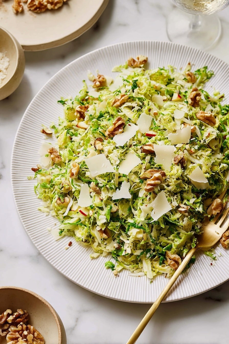 On a large white plate with a subtle ridged edge, there is a layered salad made of finely shredded bright green Brussels sprouts mixed with small pieces of red-skinned apple and light brown walnut chunks spread evenly across. Scattered on top are thin, pale off-white cheese shavings, adding a rough, slightly curled texture. A gold-colored fork rests on the plate, partially under the salad towards the lower right. The plate is set on a white marbled surface with two beige bowls blurred in the background, one with walnuts and the other with a creamy white ingredient. Photo taken with an iphone --ar 2:3 --v 7 - Shaved Brussels Sprouts Salad with Apple, Walnuts, and Parmigiano, healthy Brussels sprouts salad, easy Brussels sprouts salad recipe, flavorful vegetable salads, quick nutritious salads