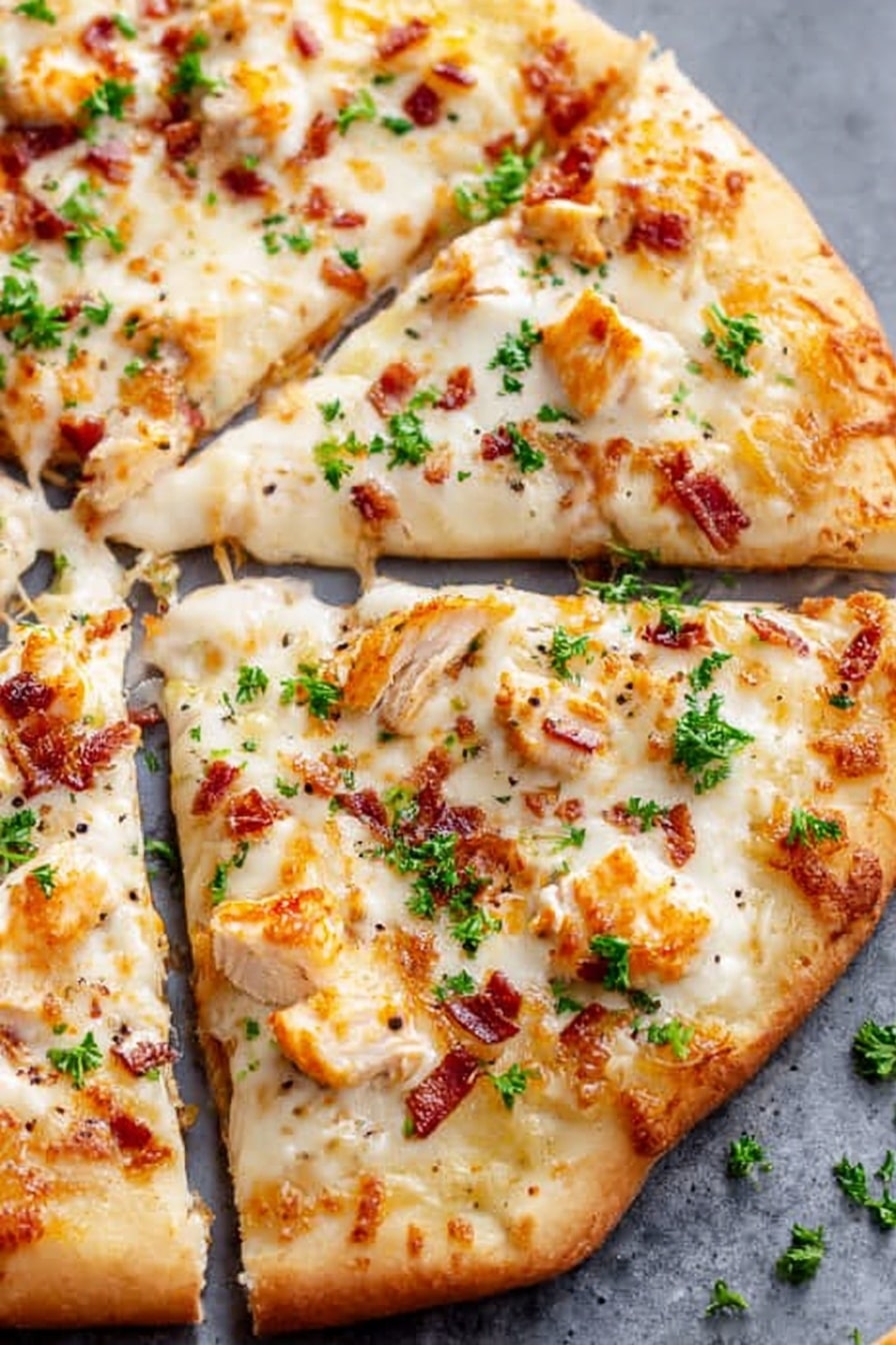 A close-up view of a pizza with four visible slices, placed on a gray surface. The pizza has two main layers: a golden-brown baked crust base showing a soft, slightly thick texture and a thick layer of melted white cheese spreading evenly across the top. Scattered on the cheese are small, light orange pieces of cooked chicken and tiny bits of reddish-brown bacon. There are bright green parsley leaves sprinkled all over, adding color contrast, and some small black pepper specks. The cheese appears smooth with a few browned spots near the edges. The overall look is warm, fresh, and cheesy. Photo taken with an iphone --ar 2:3 --v 7 - Chicken Alfredo Pizza, Creamy Alfredo Pizza, Easy Chicken Pizza, Homemade Alfredo Pizza, Cheesy Chicken Pizza