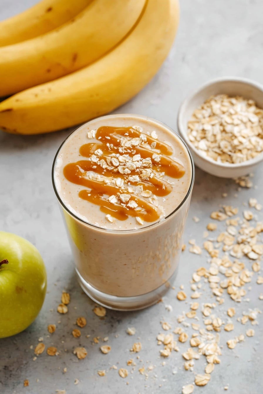 A glass filled with a light beige smoothie is topped with a drizzle of caramel-colored sauce and sprinkled with light tan oatmeal flakes. Surrounding the glass on a white marbled surface are two yellow-green apples at the bottom left and a small white bowl filled with more oatmeal flakes to the upper right. In the top left corner, a few speckled yellow bananas are partially visible. There are scattered oatmeal flakes around the glass on the surface. Photo taken with an iphone --ar 2:3 --v 7 - Apple Smoothie, healthy apple smoothie, quick breakfast smoothie, easy fruit smoothie, creamy apple banana smoothie