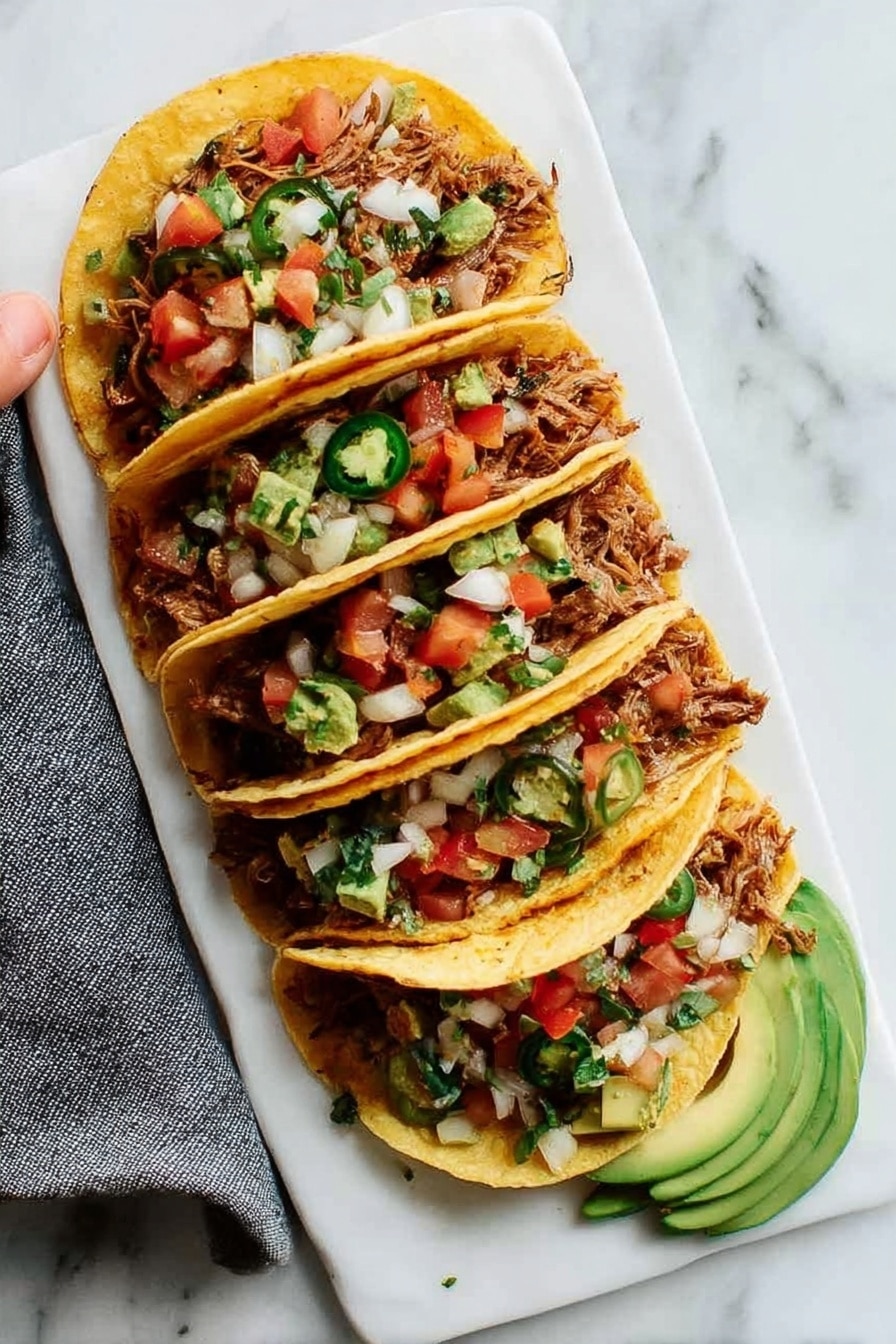 Four tacos are arranged next to each other on a white rectangular plate placed on a white marbled surface. Each taco has a golden yellow corn tortilla shell folded over a filling of shredded cooked meat with a slightly crispy texture. On top of the meat are finely chopped white onions, small diced red tomatoes, green jalapeño slices, and small green avocado pieces. Slices of avocado are placed at the bottom edge of the plate near the tacos. A woman's hand holding a gray cloth napkin is visible on the left side. The overall colors are warm and fresh with a mix of golden, green, red, and white. Photo taken with an iphone --ar 2:3 --v 7 - Easy Slow Cooker Carnitas, slow cooker pork recipes, Mexican pork dishes, tender carnitas, flavorful pork tacos