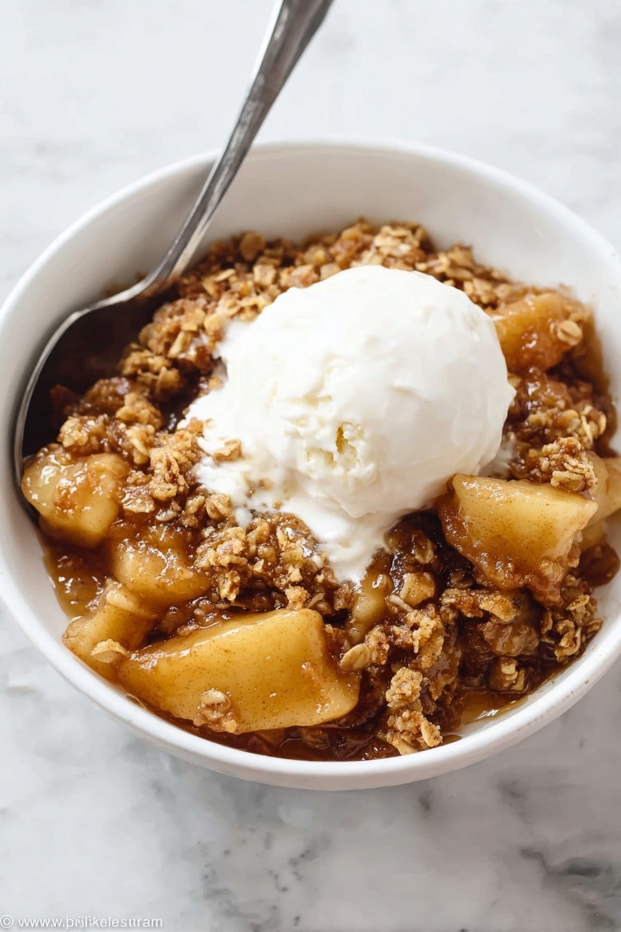A white bowl filled with warm apple crisp, showing a bottom layer of soft, caramelized golden brown apple slices coated in syrup, topped with a middle layer of crumbly, slightly rough textured oat and brown sugar crumble that looks crunchy, and finished with a generous scoop of smooth, creamy white ice cream melting over the crumble and apples. A silver spoon rests inside the bowl, partially buried in the dessert. The bowl sits on a white marbled surface. Photo taken with an iphone --ar 2:3 --v 7 - The Best Apple Crisp, apple crisp dessert, cinnamon apple crisp, easy apple crisp, comforting fall desserts