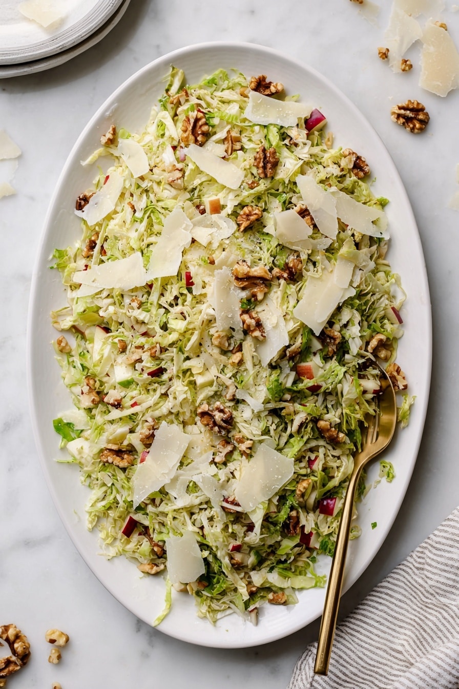 A white oval plate is filled with a colorful salad made of shredded light green cabbage mixed with small pieces of red apple, scattered walnut halves, and large thin white cheese shavings layered on top. The salad has a fresh and textured look with crunchy elements visible. A gold fork is placed inside the salad on the right side. The plate is on a white marbled surface with some shredded cheese pieces scattered around. A striped cloth napkin is placed near the bottom-right corner of the image. Photo taken with an iphone --ar 2:3 --v 7 - Shaved Brussels Sprouts Salad with Apple, Walnuts, and Parmigiano, healthy Brussels sprouts salad, easy Brussels sprouts salad recipe, flavorful vegetable salads, quick nutritious salads