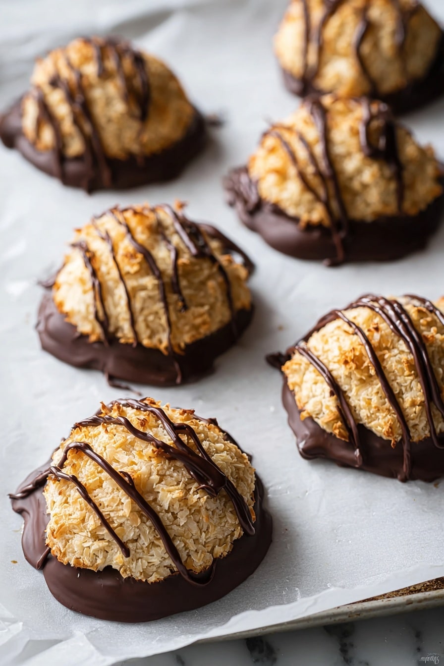 This image shows six dome-shaped cookies on a tray with white parchment paper, each cookie having two visible layers. The bottom half of each cookie is covered in dark, smooth chocolate forming a solid base layer. The top half is a rough, golden-brown toasted coconut layer with a coarse texture. Dark chocolate is lightly drizzled across the top of each cookie in thin, uneven lines. The background surface is white marbled texture. photo taken with an iphone --ar 2:3 --v 7 - Vegan Chocolate Dipped Pumpkin Macaroons, gluten-free fall treats, vegan pumpkin dessert recipes, healthy pumpkin snacks, chocolate-dipped coconut macaroons