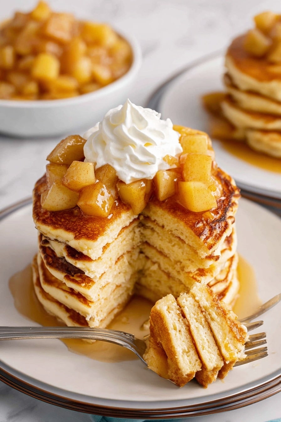 A stack of seven thick pancakes with warm golden-brown sides sits on a white plate with a thin dark rim. The pancakes are topped with soft, diced cooked apples in a light syrup, and a white swirl of whipped cream sits on top of the apples. A piece of the pancake stack is cut out, showing the fluffy light-yellow inside of the pancakes in about seven layers. A silver fork holds a bite-sized stack of four pancake pieces with a small apple chunk. In the background, a bowl filled with more cooked apple chunks and another plate with more pancakes and cooked apples are visible. All are placed on a white marbled surface. Photo taken with an iphone --ar 2:3 --v 7 - Apple Pancakes, cinnamon apple pancakes, fluffy apple pancakes, easy apple pancake recipe, breakfast with apples