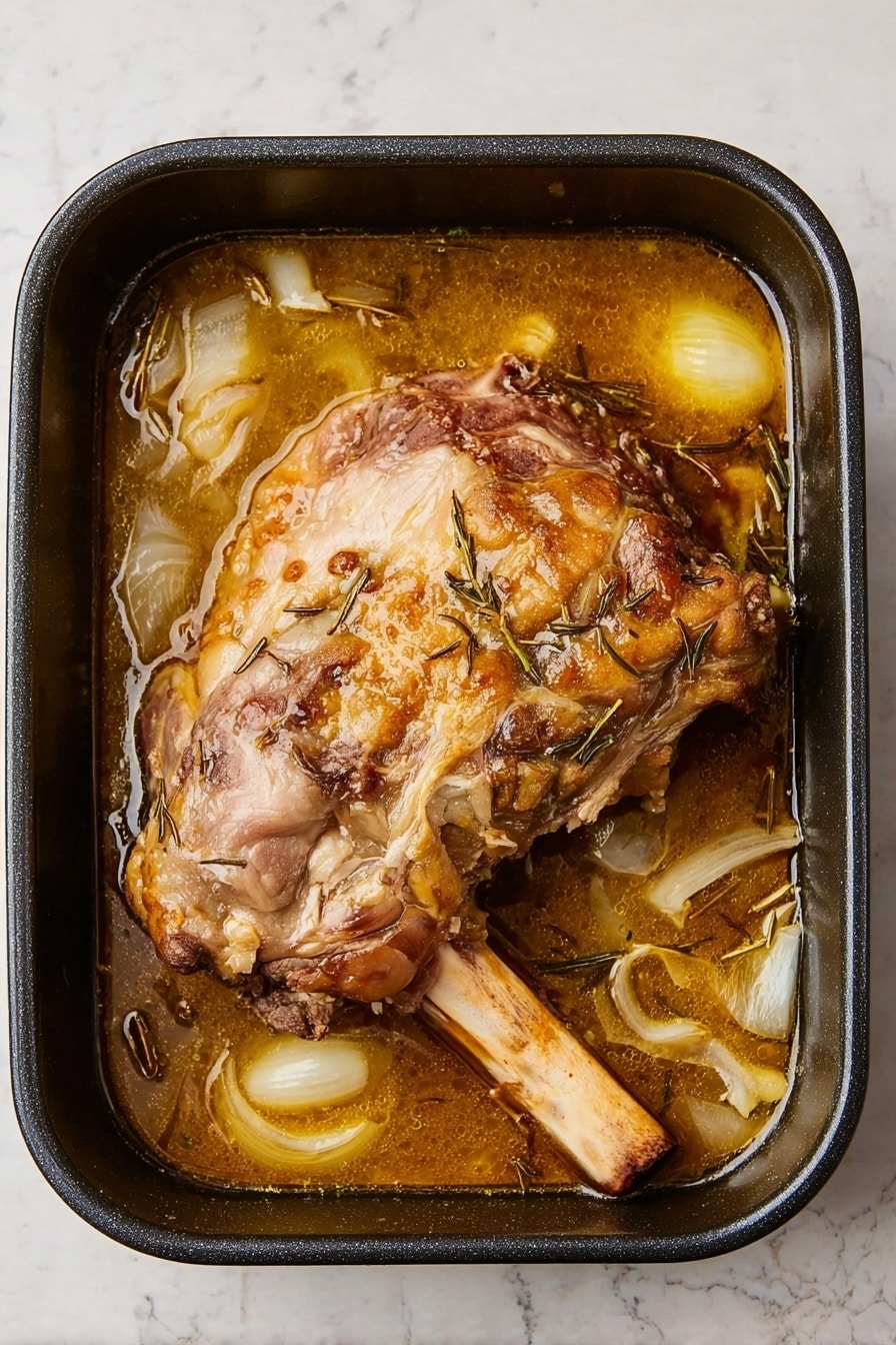 The image shows a black roasting pan filled with a large cooked meat piece, mainly beige and brown with some crisped golden brown spots, sitting in a light brown broth. The broth contains large chunks and slices of translucent white onions and visible thin sprigs of herbs scattered throughout. The pan rests on a white marbled surface that adds a clean, bright contrast to the warm colors of the meat and broth. The texture of the meat looks tender and slightly browned on the edges, with the long bone extending out to the right side. Photo taken with an iphone --ar 2:3 --v 7 - Slow Roast Leg of Lamb with Garlic, Rosemary, and Rich Pan Juices, roasted leg of lamb with garlic and rosemary, tender slow roast lamb recipe, flavorful roast lamb dishes, easy lamb roast for special occasions