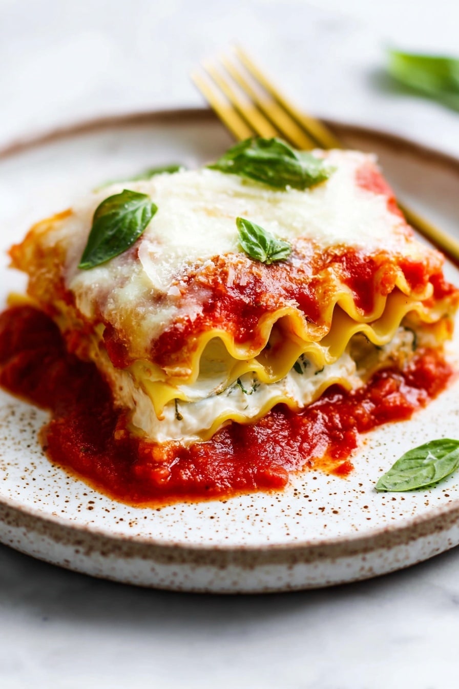 A single rolled lasagna is placed on a white plate with brown speckles, sitting on a white marbled surface. The lasagna has multiple layers visible on the side: pale yellow pasta sheets folded with creamy white cheese filling inside. It is covered with bright red tomato sauce that pools around the base and melted white cheese layered on top, slightly browned in spots. A few fresh green basil leaves are placed on top as garnish. A gold fork is partially visible behind the lasagna. Photo taken with an iphone --ar 2:3 --v 7 - Lasagna Roll-Ups with Kale Ricotta and Mozzarella, baked lasagna roll-ups, healthy lasagna roll-ups, easy Italian pasta dishes, vegetarian lasagna roll-ups