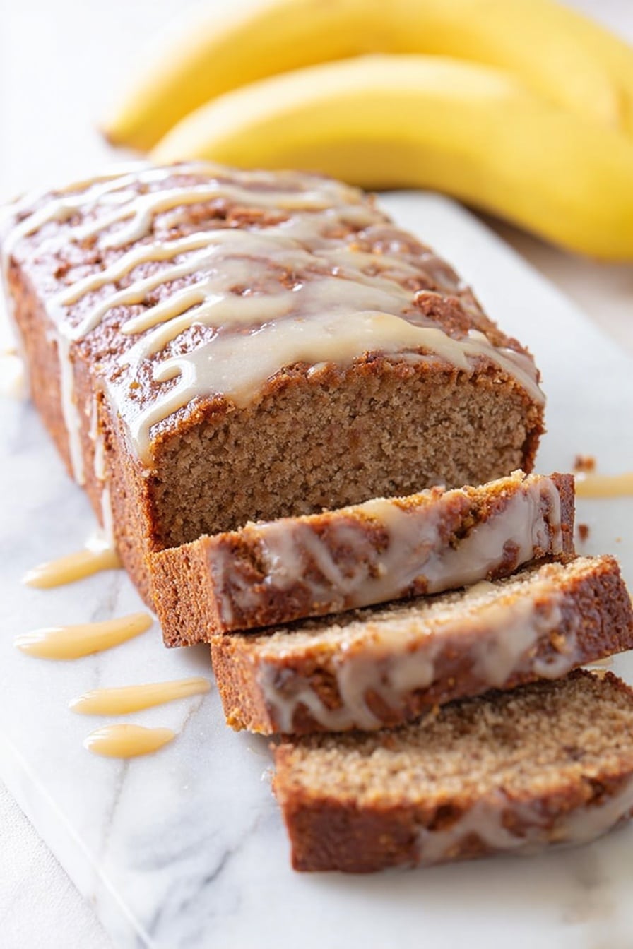 A loaf of dark brown chocolate bread sits on a white marbled surface, with a thick drizzle of light brown caramel sauce running down the top and sides, creating shiny streaks. In the background, there is a bunch of yellow bananas and a white bowl filled with more caramel sauce, softly blurred. The bread looks moist with visible cracks on the top where the caramel pools slightly. Photo taken with an iphone --ar 2:3 --v 7 - Dulce de Leche Banana Bread, decadent banana bread with dulce de leche, moist banana bread recipe, easy banana bread with caramel, sweet banana bread treat