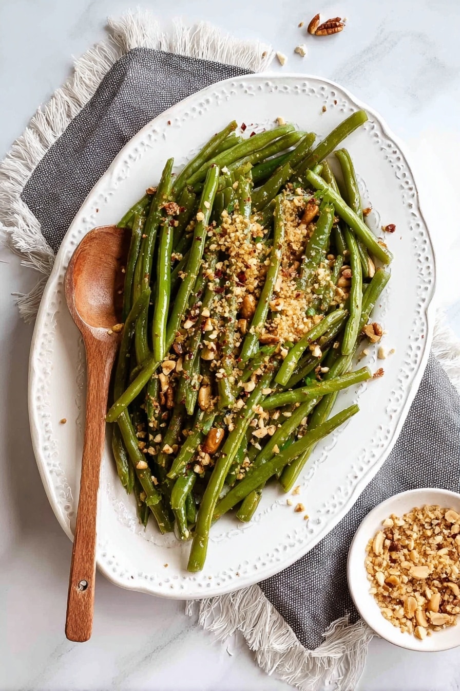 The image shows a white, oval plate with a lacy edge holding a pile of cooked green beans arranged loosely. The green beans are long and slender, topped with a layer of crushed nuts and some crushed red pepper flakes, adding a mix of light brown, orange, and beige colors on top. A wooden spoon rests on the left side of the plate over the beans. To the right of the plate, there is a small white bowl filled with more crushed nuts. The whole setup sits on a white marbled surface with a fringed gray cloth partially under the plate. The photo taken with an iphone --ar 2:3 --v 7 - Instant Pot Green Beans with Garlic and Almonds, healthy green bean side dish, quick vegetable recipes, easy garlic green beans, flavorful green bean side dish