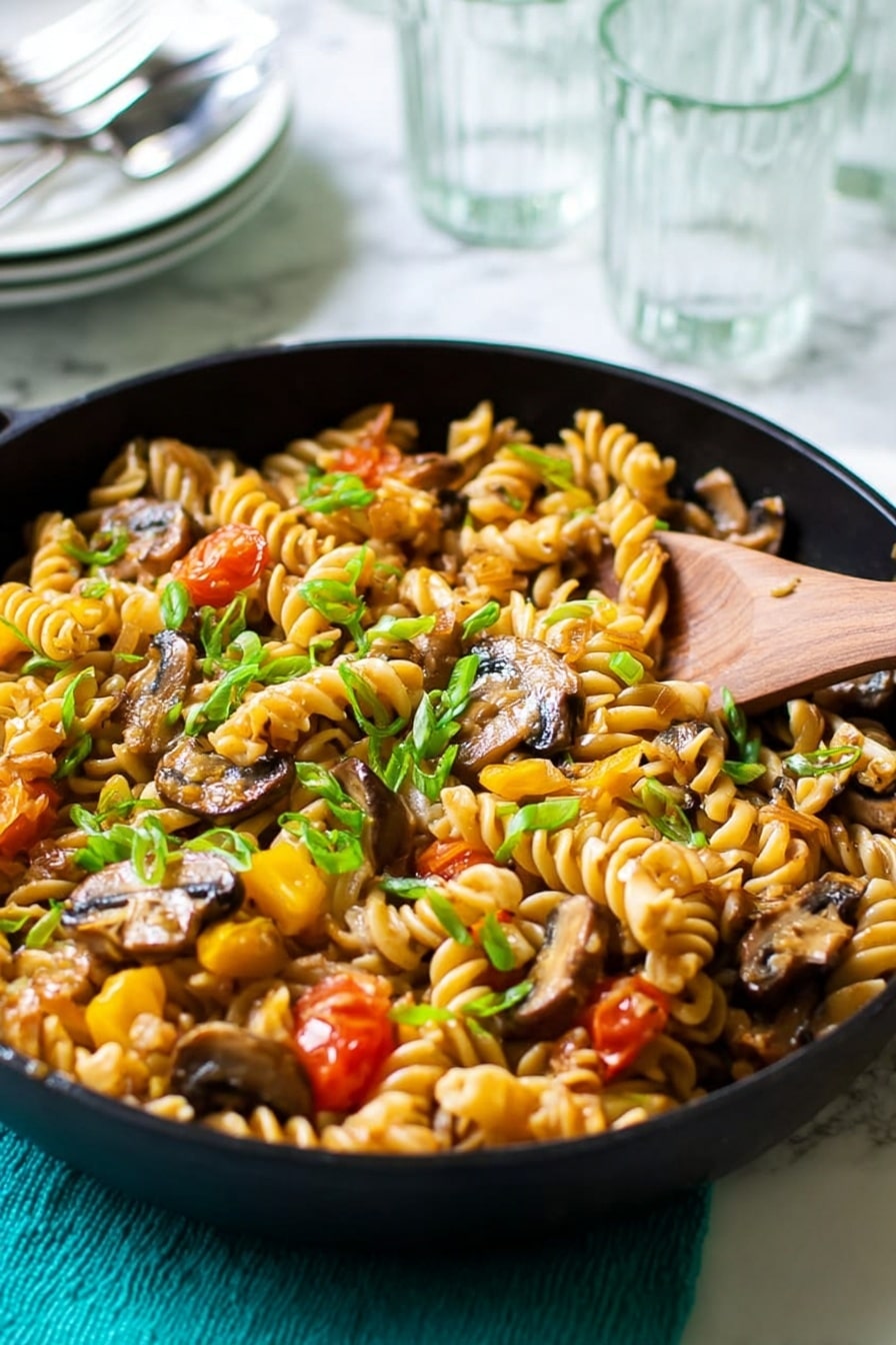 A close-up view of a black skillet filled with cooked rotini pasta mixed with sliced mushrooms, diced yellow bell peppers, and cherry tomatoes; the dish is topped with finely chopped green onions. A wooden spoon rests on the right side of the skillet, partially stirring the pasta. The skillet sits on a teal textured cloth, set on a white marbled surface. In the blurry background, there are transparent drinking glasses and a stack of white bowls with silver cutlery on top. Photo taken with an iphone --ar 2:3 --v 7 - Fusilli with Mushroom and Roasted Butternut Squash, autumn pasta dish, healthy mushroom and butternut squash pasta, wholesome fusilli with roasted squash, vegetarian fall pasta