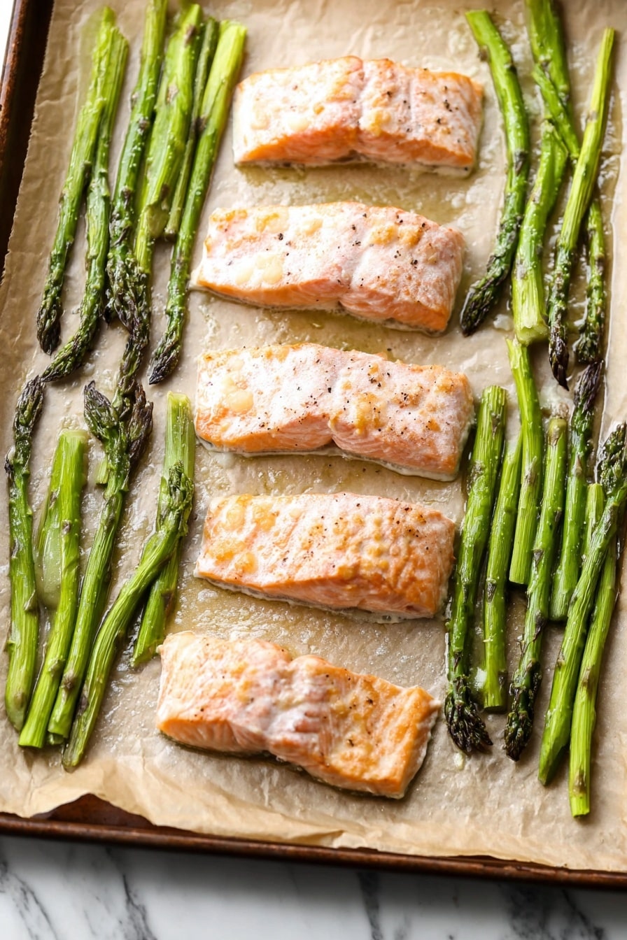 The image shows a close-up of a cooked salmon fillet on a white plate, placed on a white marbled surface. The salmon is light pink with a slightly bubbly, shiny top layer of melted butter or sauce, with small bits of garlic and black pepper visible. Next to the salmon, on the right side, are several bright green asparagus spears with a slight shine, showing light grill marks and smoky texture. The overall dish has a fresh and simple look with a clean presentation. photo taken with an iphone --ar 2:3 --v 7 - One-Pan Baked Salmon and Asparagus, baked salmon asparagus, healthy salmon dinner, easy salmon recipes, quick weeknight salmon